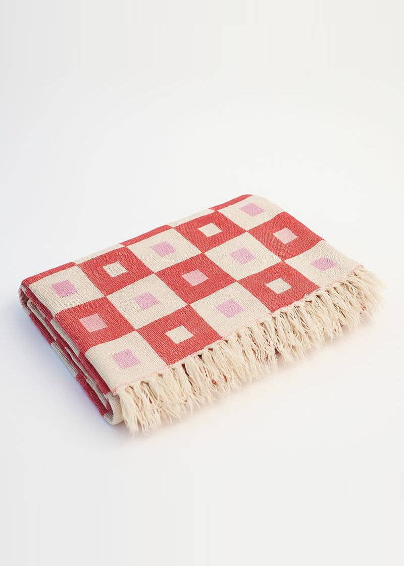 Checkered blanket with pink and red squares and beige fringe on a white background